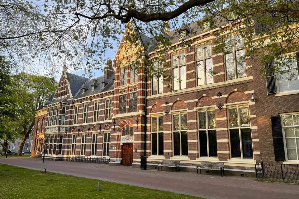 Historisch bakstenen gebouw met hoge ramen aan een plein met bomen in het centrum van Assen
