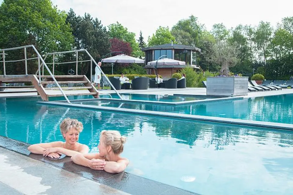 Twee gasten ontspannen aan de rand van het buitenbad van een spa in de omgeving van Drentse Vennen