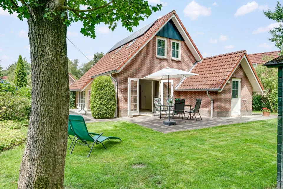 Bakstenen vakantiewoning Zanglijster 17 met terras, parasol en ligstoel op een groot grasveld