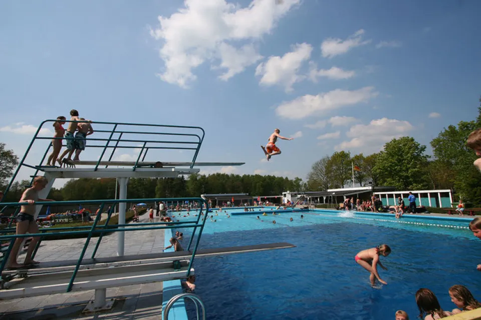 Buitenzwembad met duikplanken en zwemmers onder een blauwe lucht in Haulerwijk