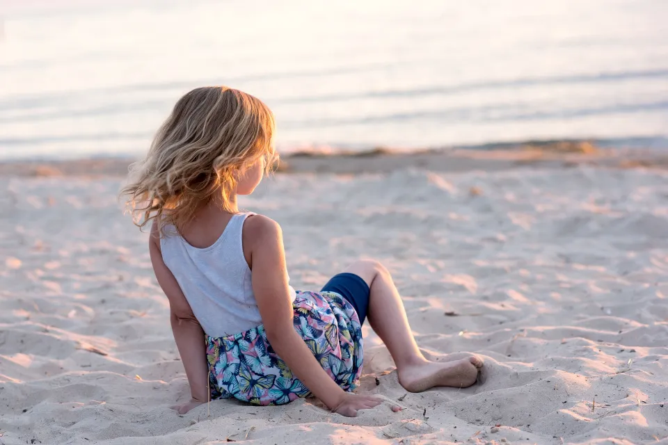 Jong meisje zit in het zand op het strand bij het water in de omgeving van Drentse Vennen